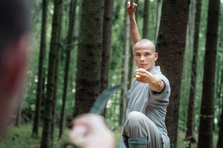 Men in gray clothes practicing kung fu with stick and sword during training in woods