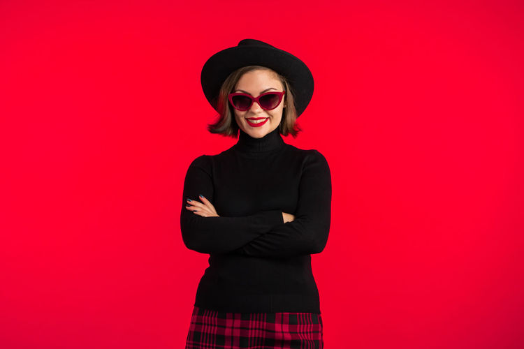 Woman wearing sunglasses standing against red background