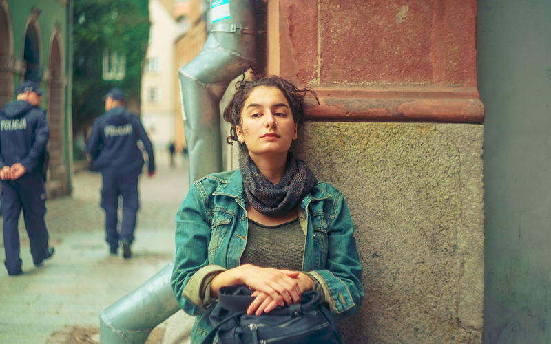 Tired woman sitting against wall at sidewalk