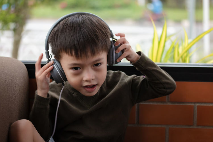Portrait of boy wearing headphones while sitting against brick wall