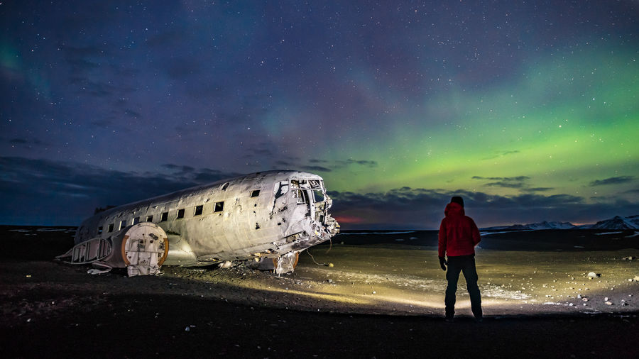 Rear view of man looking at abandoned ship in sea against sky during night
