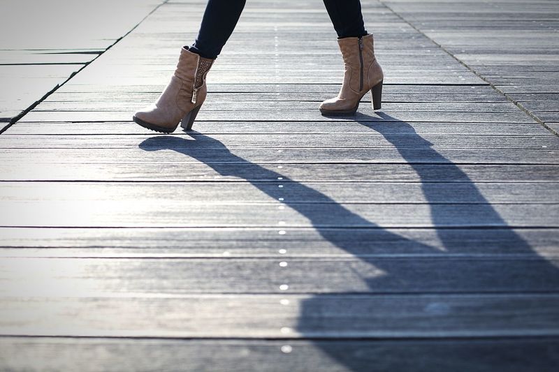 Legs of woman in ankle boots walking on boardwalk
