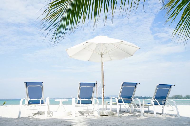 Lounge chairs and tables on beach against sky