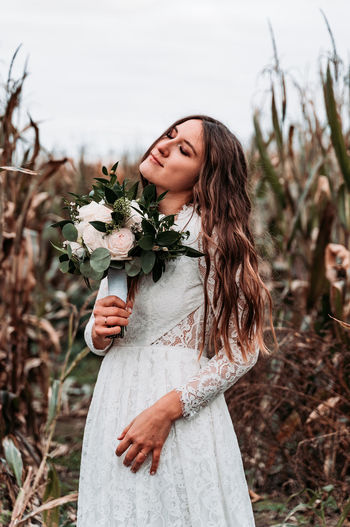 Bride holding flower while standing on land against sky