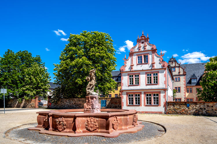 Fountain by building against blue sky
