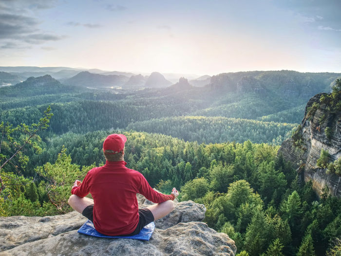 Man meditates in yoga position in mountains above wild nature at sunset. concept of meditation