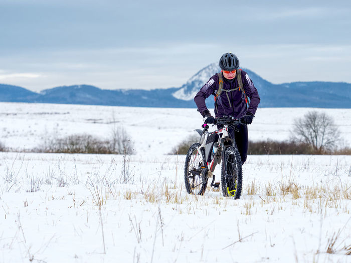 Biker is pushing  mtb through the snow across a frozen meadow. hard terrain, the biker can't ride.