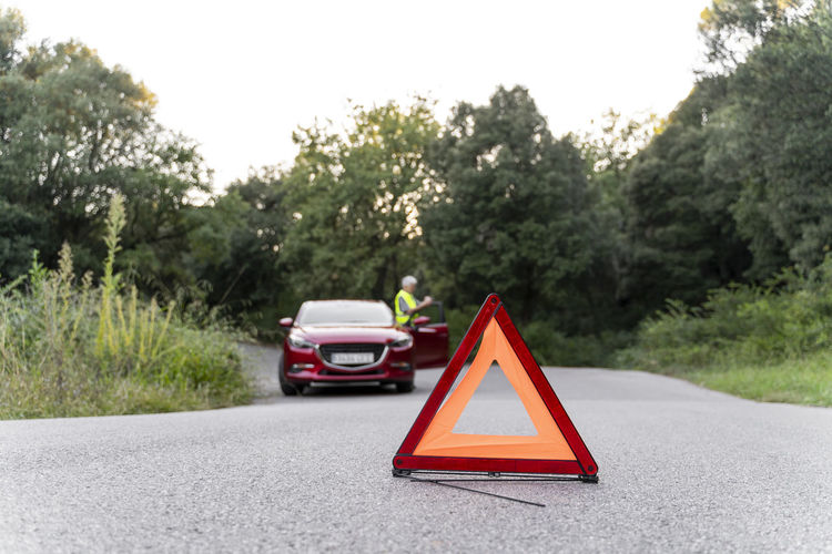 Warning triangle in front of a senior man's broken car on a country road