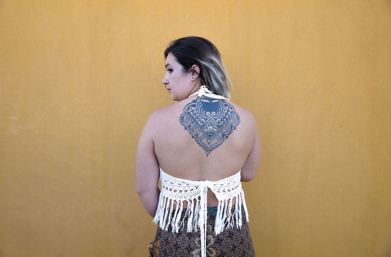 Rear view of young girl showing her tattoo in back against yellow wall
