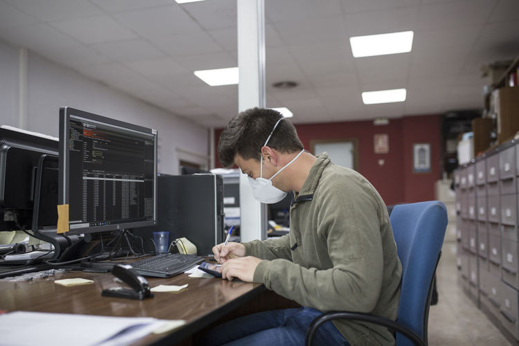 Side view of businessman wearing mask working at desk in office