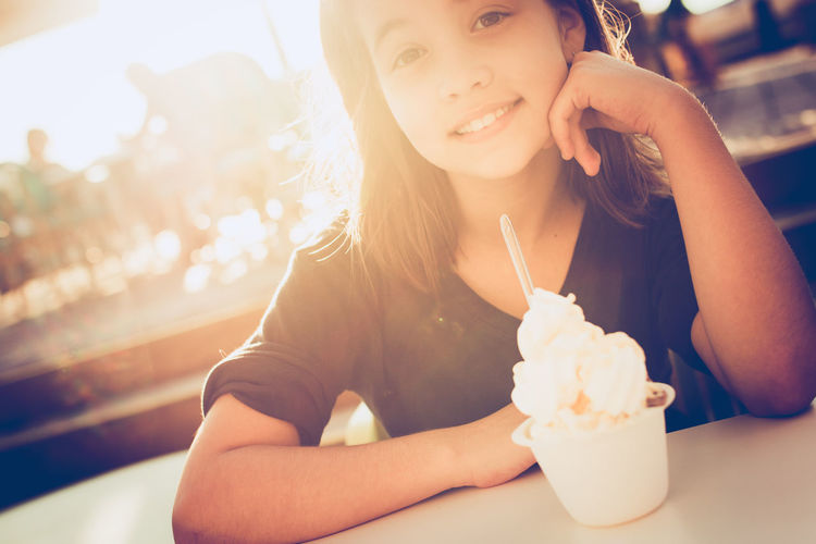 Tilt portrait of happy girl with ice cream served on table at restaurant