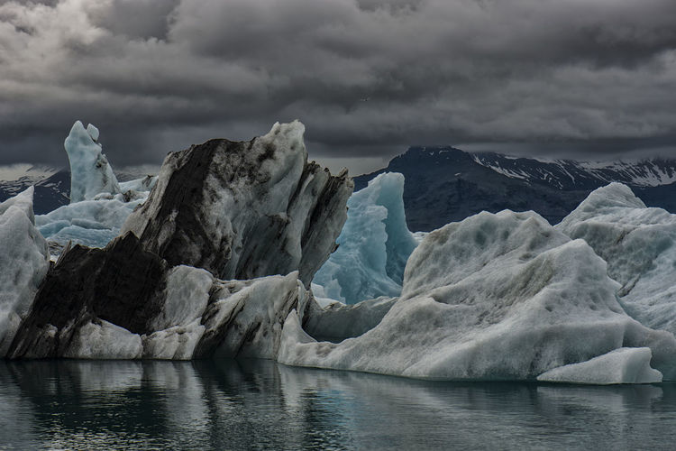 Scenic view of icebergs in sea against cloudy sky
