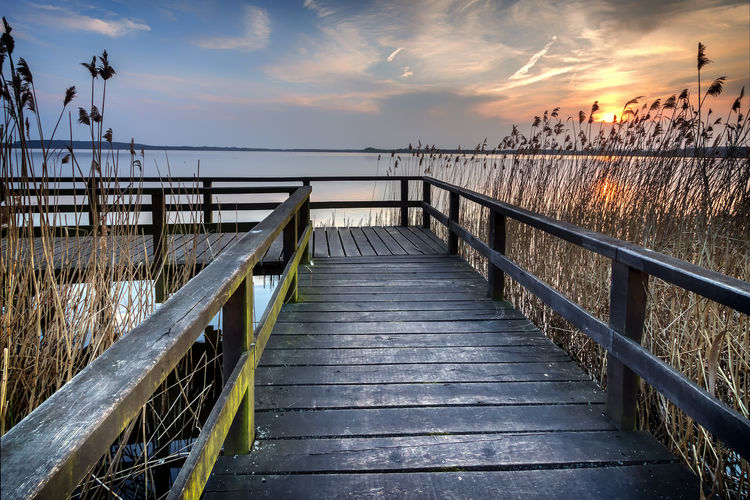 Boardwalk amidst sea against sky during sunset