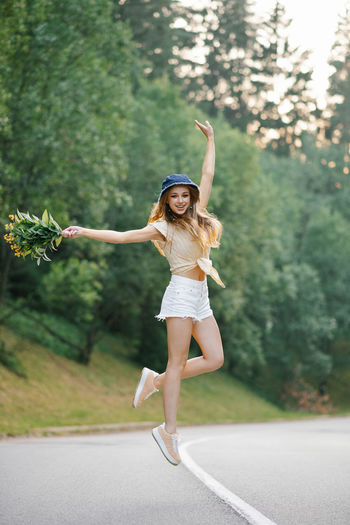 A happy girl in white shorts and a yellow blouse jumps up with a bouquet of flowers