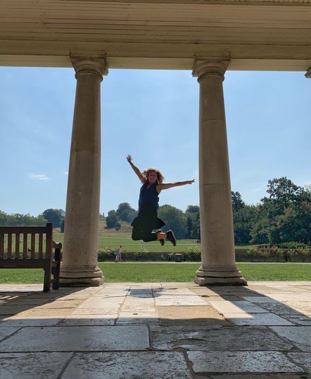 Woman with arms outstretched jumping by columns