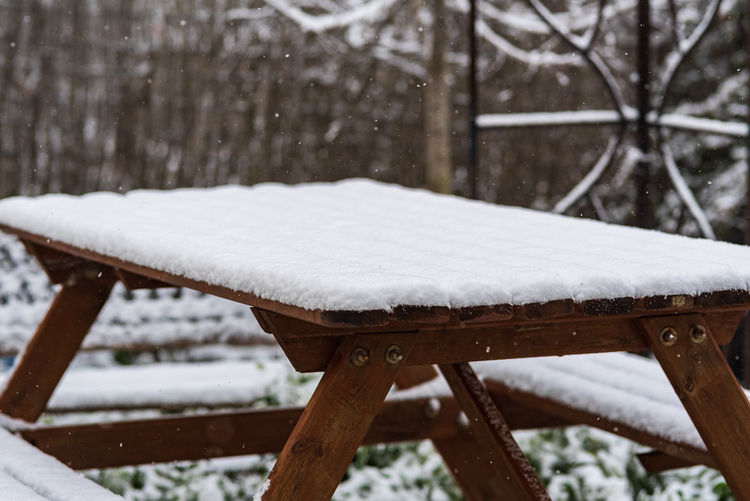 Snow covered bench on wooden table during winter