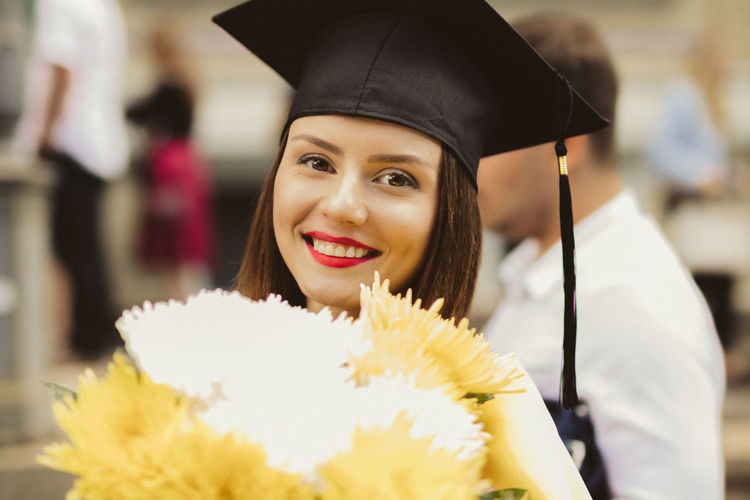 Portrait of smiling young woman with mortarboard and bouquet