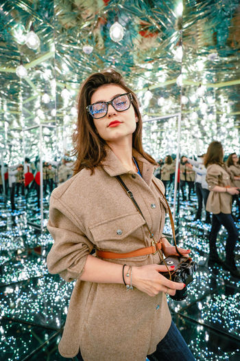 Portrait of young woman standing against illuminated christmas
