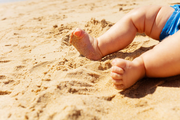 Low section of baby on sand at beach