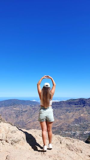 Landscape view with a girl making heart with hands. canary island roque nublo, spain. 