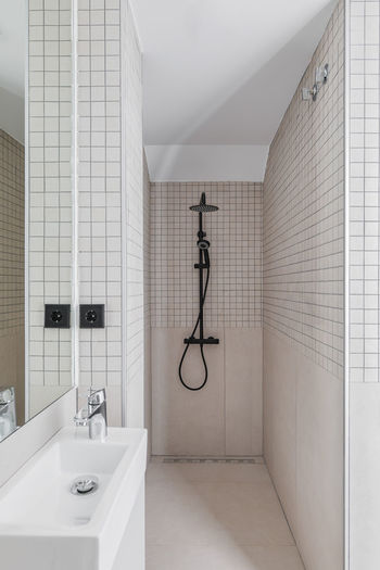 Narrow bathroom with shower zone and small sink. interior of modern bathroom with beige tiles.