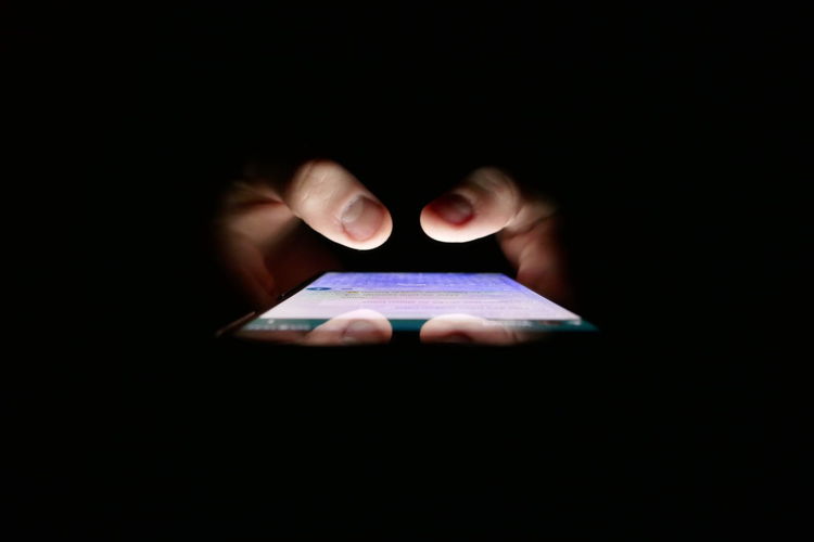 Close-up of hands using mobile phone against black background
