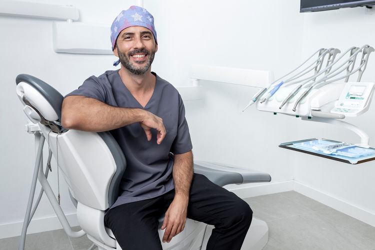 Portrait of a male dentist with uniform leaning on a stretcher in a dental clinic