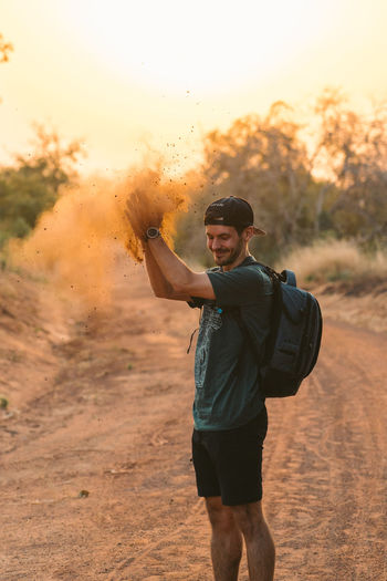 Young man throwing dirt while standing on dirt road