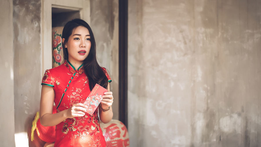Beautiful young woman holding envelop standing against wall