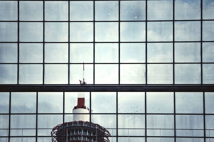 Low angle view of kyoto tower seen through modern glass building