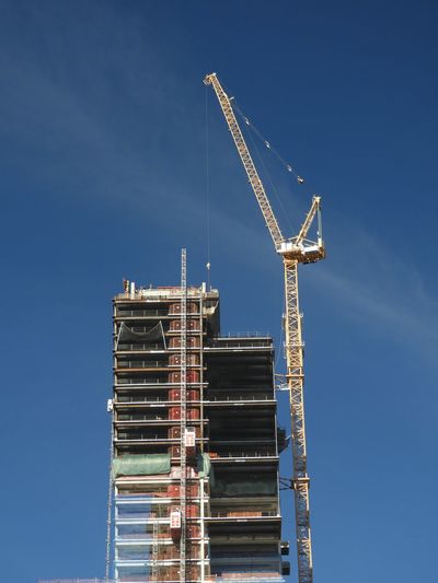 Low angle view of crane at under construction building against blue sky