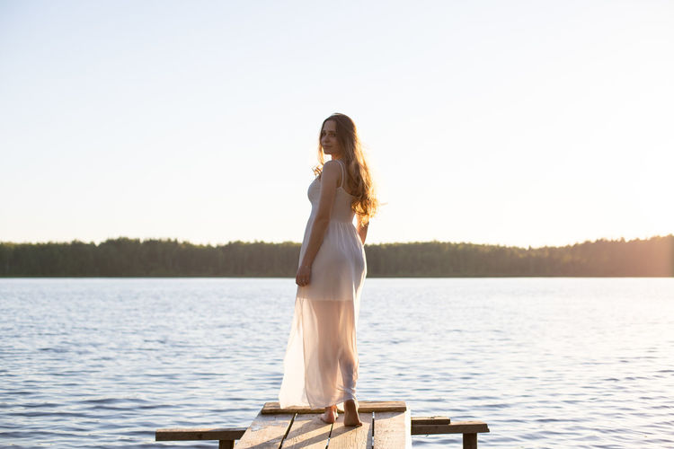 Rear view of woman standing by lake against clear sky