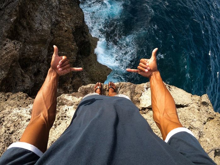 Low section of man gesturing shaka sign against sea