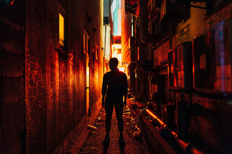 Full length of man standing in alley amidst buildings at night