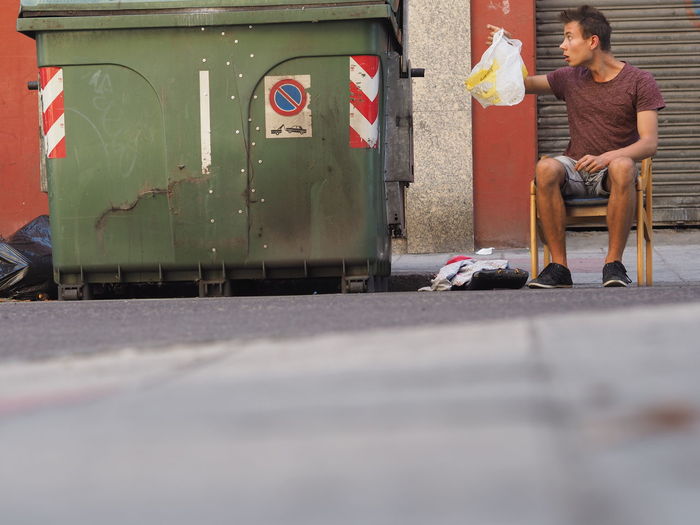 Surface level of young man looking at plastic bag by garbage bin