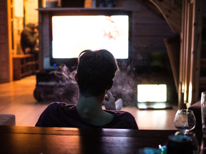 Rear view of man smoking while watching television at home
