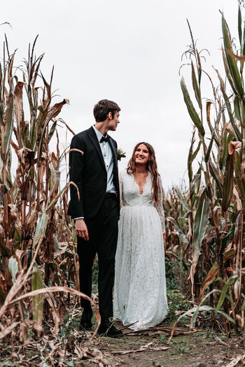 Newlywed couple standing amidst plants against clear sky