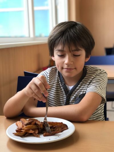 Boy having potato chips while sitting on chair at restaurant