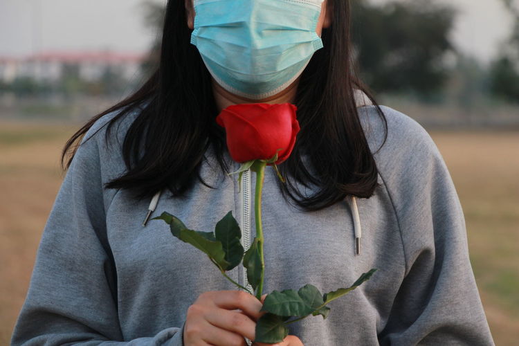 Midsection of woman holding rose while wearing mask outdoors