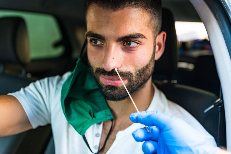 Taking a nasal swab from a man in car to test for coronavirus infection - a healthcare worker operat