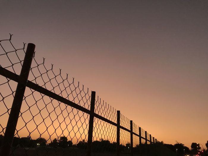 Low angle view of silhouette fence against sky during sunset