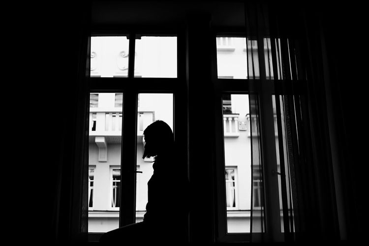 Silhouette woman standing by window at home