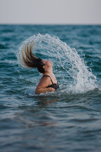 Woman splashing water while tossing hair in sea