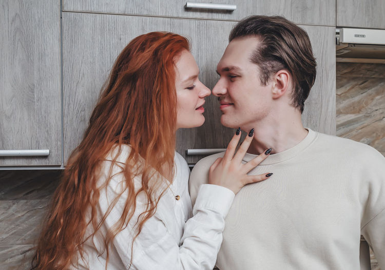 Romantic conversation in kitchen of two lovers. red-haired girl passionately touches boyfriend.