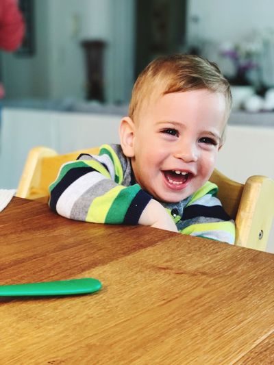 Cheerful baby boy looking away while sitting at table in home