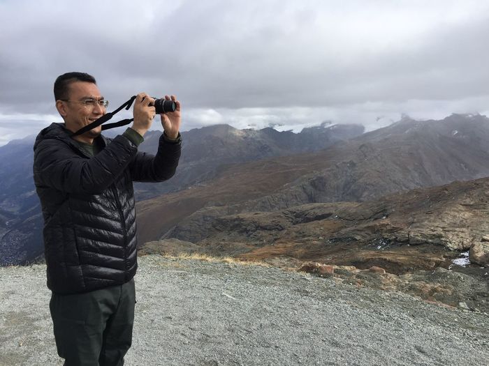 Man photographing on land against cloudy sky