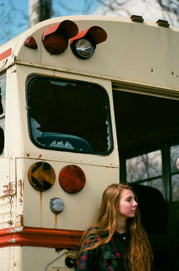 Young woman standing by an abandoned school bus