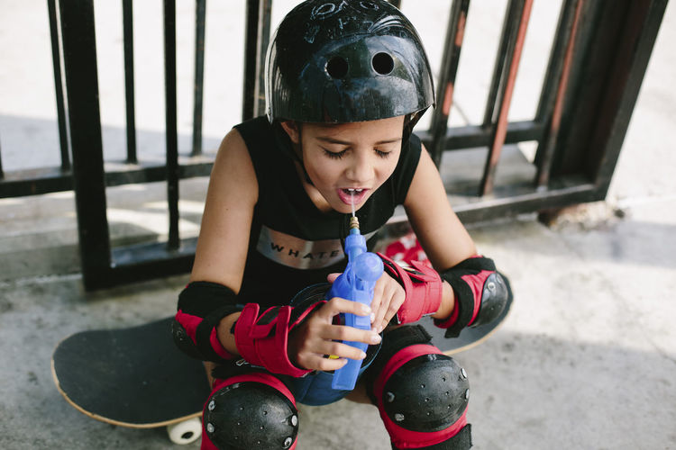 High angle view of tired girl drinking water while sitting on skateboard
