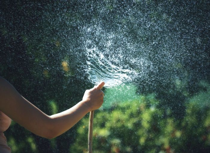 Midsection of woman spraying water with garden hose