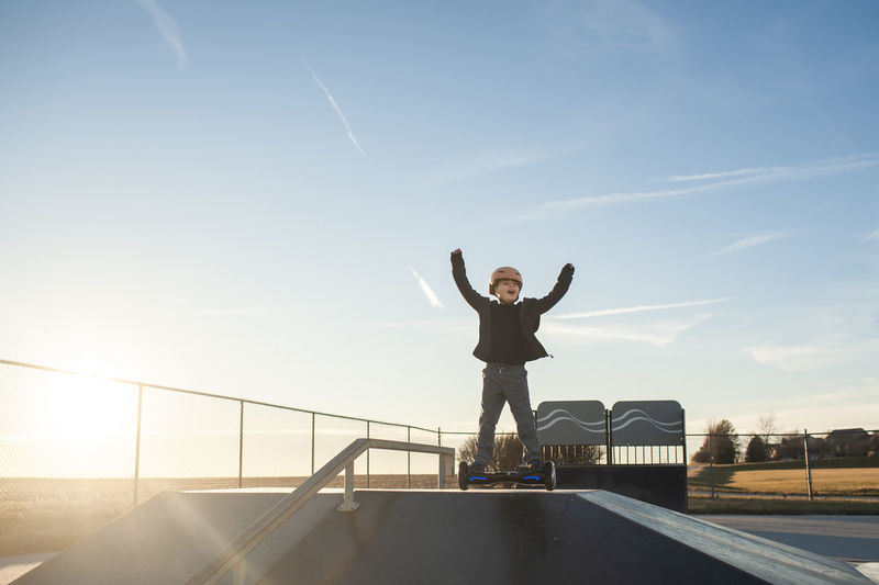 Young boy celebrating on hoverboard on top of ramp at skate park